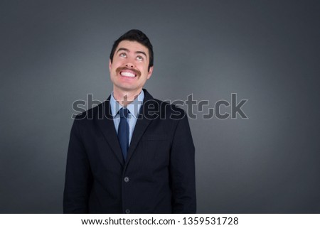 Portrait of mysterious charming businessman looking up with enigmatic smile. Handsome smiling guy looking up standing against gray wall.
