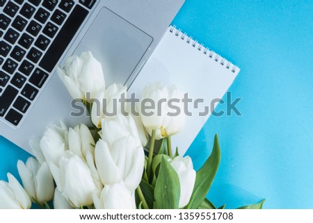 Top view of a laptop with blue tulips and a white notepad. The desktop is female, flat lay. Surprise. Planning. Present. Be in love. Place for text. Template