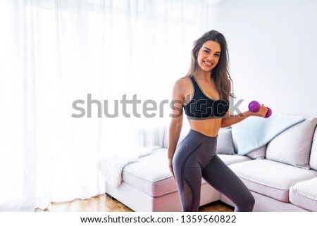 Cheerfully smiling mixed race sporty woman demonstrating biceps, isolated on white background. Sporty woman does the exercises with dumbbells. Photo of muscular woman in sportswear.
