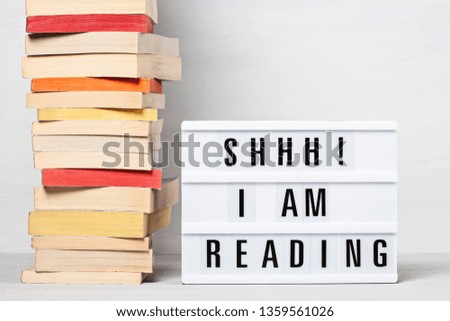 Heap of books and light box with the text I am reading