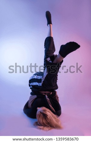 Attractive woman with legs in air and sports tracksuits shows his gymnastic skills on colorful background and studio red and blue lights. Low key setup