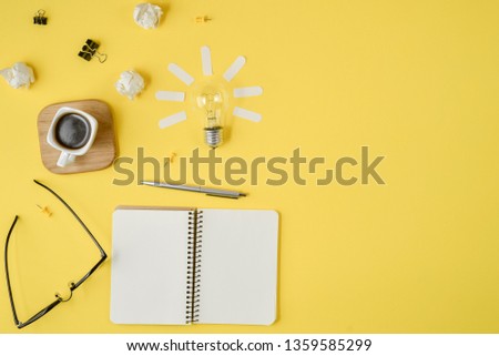 Flat lay financial planning brainstorming messy table top image with blank clip board, office supplies, pen, notepad, eyeglasses, cup of coffee, light bulb on yellow background.