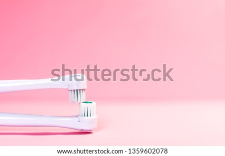 Two electrical toothbrushes on a soft light pink background.