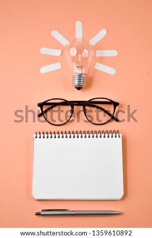 Financial planning table top with pen, notepad, eyeglasses and light bulb on orange background. Concept brainstorming and new idea