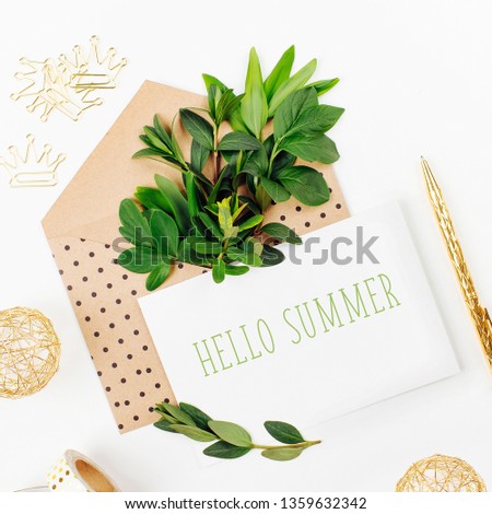 Styled desk with envelope, blank card, composition of green leaves and gold office stuff. Flat lay.