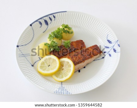 Grilled salmon fish filets on a plate with Potatoes, parsley and slices of lemon. Close up stock photo with white background.