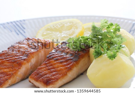 Grilled salmon fish filets on a plate with Potatoes, parley and slices of lemon. Close up stock photo with white background.