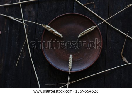 three wheat spikelets on a clay plate on a black burnt wooden background
