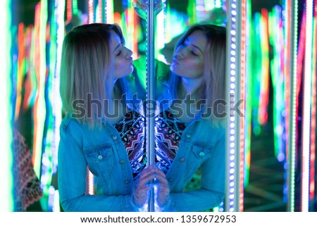 sweet caucasian girl walks in a mirror maze with colorful diodes and enjoys an unusual attraction room in the city