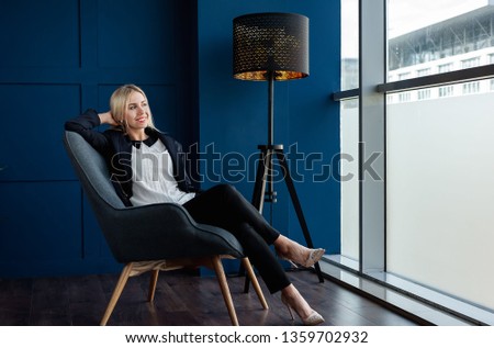
young beautiful girl in a strict suit sitting in a chair and looking out the window