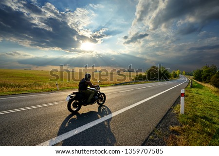 Motorcycle driving on the asphalt road in rural landscape at sunset with dramatic clouds                                Royalty-Free Stock Photo #1359707585