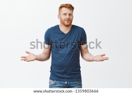 Man pretends he know anything, shrugging, making clueless expression. Portrait of unaware handsome masculine redhead male with bristle, holding hands aside, smiling, feeling confused and uncertain