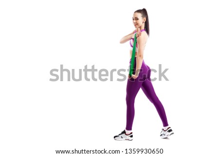 A young woman coach in a sporty purple  short top and gym leggings exercise for your  hands  with sport fitness rubber bands on a  white isolated background in studio 