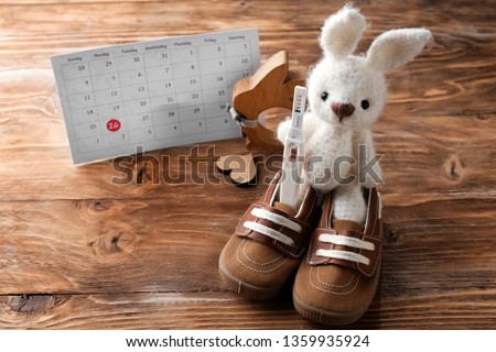 Baby booties, toy rabbit, pregnancy test and calendar on wooden background