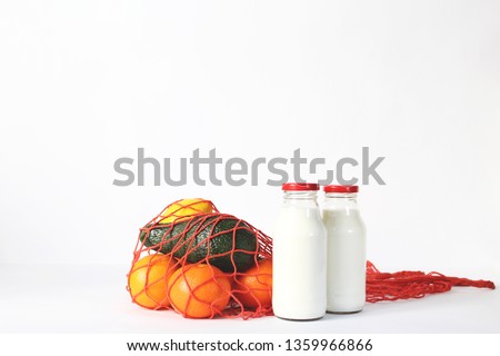 isolated red net bags for shopping and reusable glass bottle of fresh milk on white background. concept of eco friendly and zero waste .