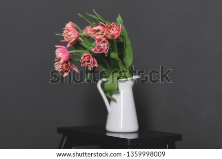 A bouquet of pink peony tulips in a white jug stand on a black bench.