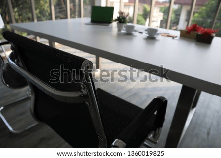 The picture of office with two black chairs and white table. Cups and laptop place on the table with others.  As an office for recruiting and interview the new applicants