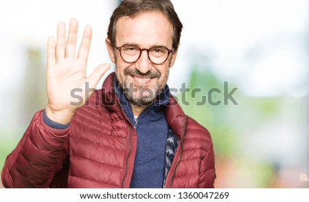 Middle age handsome man wearing glasses and winter coat Waiving saying hello happy and smiling, friendly welcome gesture