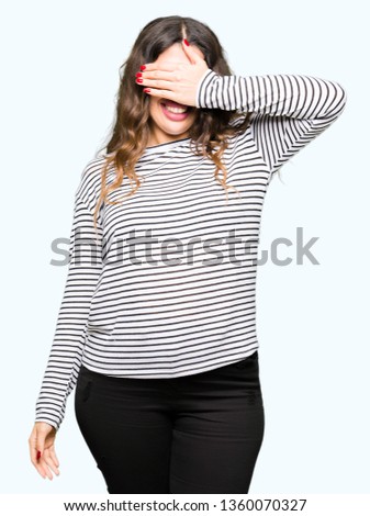Young beautiful woman wearing stripes sweater smiling and laughing with hand on face covering eyes for surprise. Blind concept.