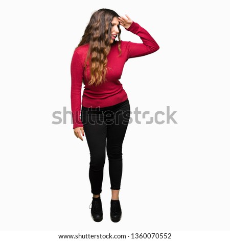 Young beautiful woman wearing red sweater very happy and smiling looking far away with hand over head. Searching concept.