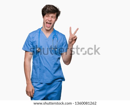 Young doctor wearing medical uniform over isolated background smiling with happy face winking at the camera doing victory sign. Number two.