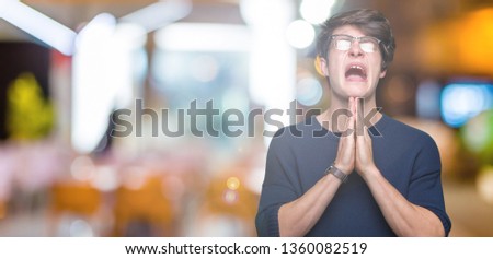 Young handsome man wearing glasses over isolated background begging and praying with hands together with hope expression on face very emotional and worried. Asking for forgiveness. Religion concept.
