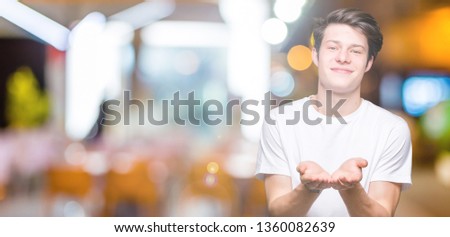 Young handsome man wearing casual white t-shirt over isolated background Smiling with hands palms together receiving or giving gesture. Hold and protection