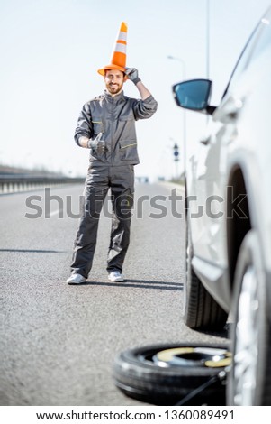Funny portrait of a road assistance worker with emergency cone near the car on the highway