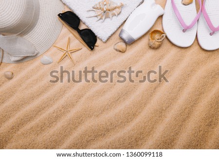 Top view of sandy beach with towel frame and summer accessories. Background with copy space and visible sand texture. left border made of towel