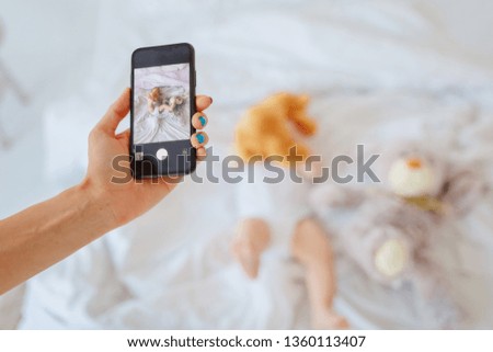 Mom makes a photo of the baby lying on the bed on the phone / copy space
