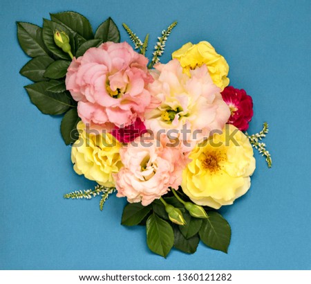 Bunch of summer pink and yellow garden flowers and leaves. Flower arrangement on elegant blue backdrop. Floral flat lay.