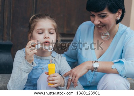 little girl blowing soap balloons wit her mother in the city