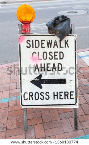 SIDEWALK CLOSED sign with yellow flashing warning light and shabby sandbag.