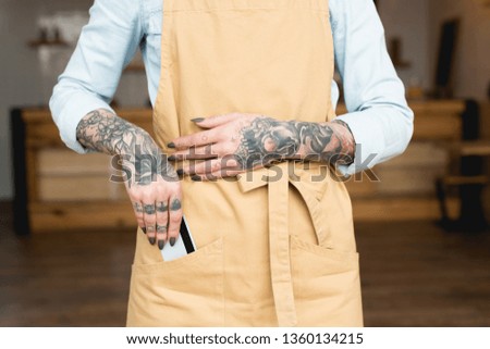 partial view of tattooed waitress putting credit card in apron pocket