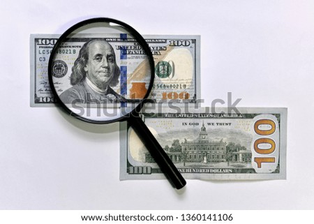 One hundred dollars under a magnifying glass. Front and back side. On a light background.