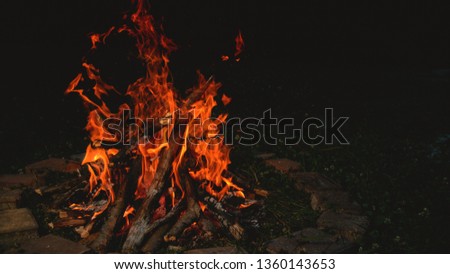 CLOSE UP: Large bright orange campfire burning inside a brick enclosed fire pit on a tranquil summer night. Bonfire providing heat and light in the campgrounds. Close up shot of a burning bonfire.