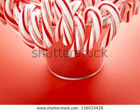 White and red peppermint candy canes in bucket on red background.