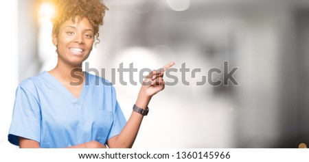 Young african american doctor woman over isolated background with a big smile on face, pointing with hand and finger to the side looking at the camera.