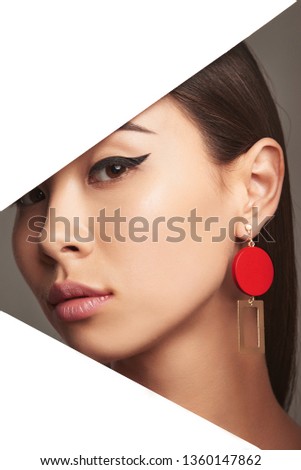Cropped closeup side portrait of girl with black flicks, tilting head behind triangle-shaped foreground. The young woman with her eyes closed is wearing dangle earrings in view of geometric figure.