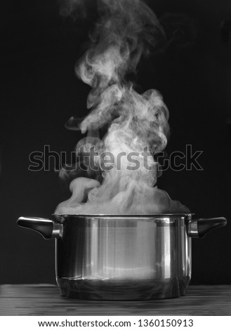 Steaming pot on black background. Smoke above boiling soup pot.  Royalty-Free Stock Photo #1360150913