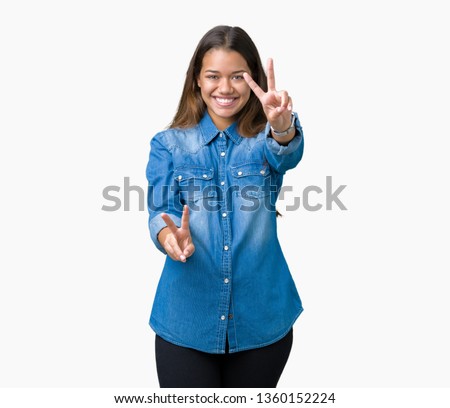 Young beautiful brunette woman wearing blue denim shirt over isolated background smiling looking to the camera showing fingers doing victory sign. Number two.
