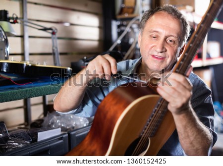 Adult glad cheerful  music master is repairing music instruments in workshop.