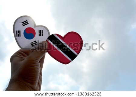 Hand holds a heart Shape South Korea and Trinidad and Tobago flag, love between two countries