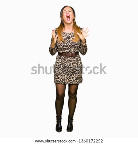 Beautiful middle age woman wearing leopard animal print dress crazy and mad shouting and yelling with aggressive expression and arms raised. Frustration concept.