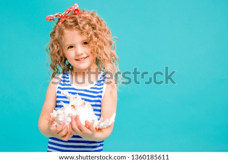 baby girl in striped t-shirt with seashell on blue background. the concept of a holiday by the sea