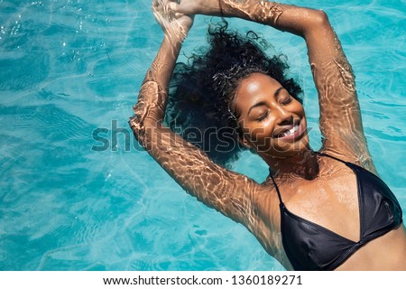 High angle view of black woman relaxing in the water with closed eyes. Portrait of happy woman in bikini floating in a water. Top view of relaxed african girl in swimming pool with copy space.