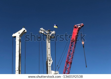 three industrial construction tower cranes with Ukrainian flags against a blue sky. building site and architecture development concept.
