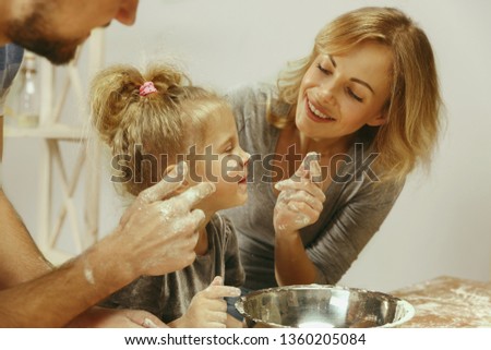 Cute little girl and her beautiful parents preparing the dough for the cake in kitchen at home. Family lifestyle concept