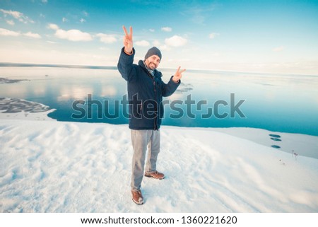 Smiling energetic young man by the sea on winter snow showing a peace sign
