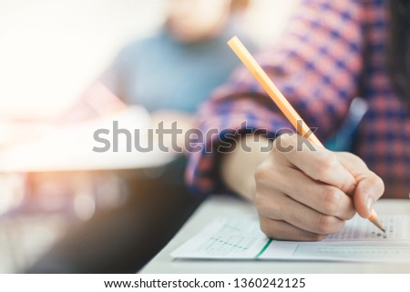 high school or university student holding pencil writing on paper answer sheet.sitting on lecture chair taking final exam attending in examination room or classroom.student in uniform Royalty-Free Stock Photo #1360242125